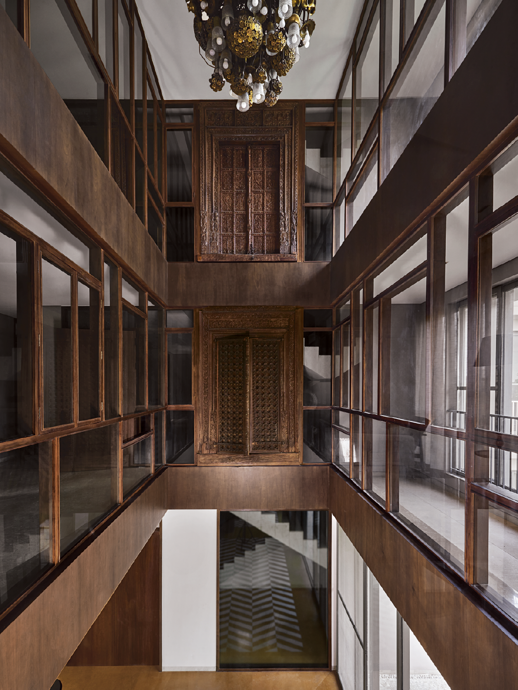 Multi-storey interior atrium with mirrored glass panels and dark timber screens in Kolkata home